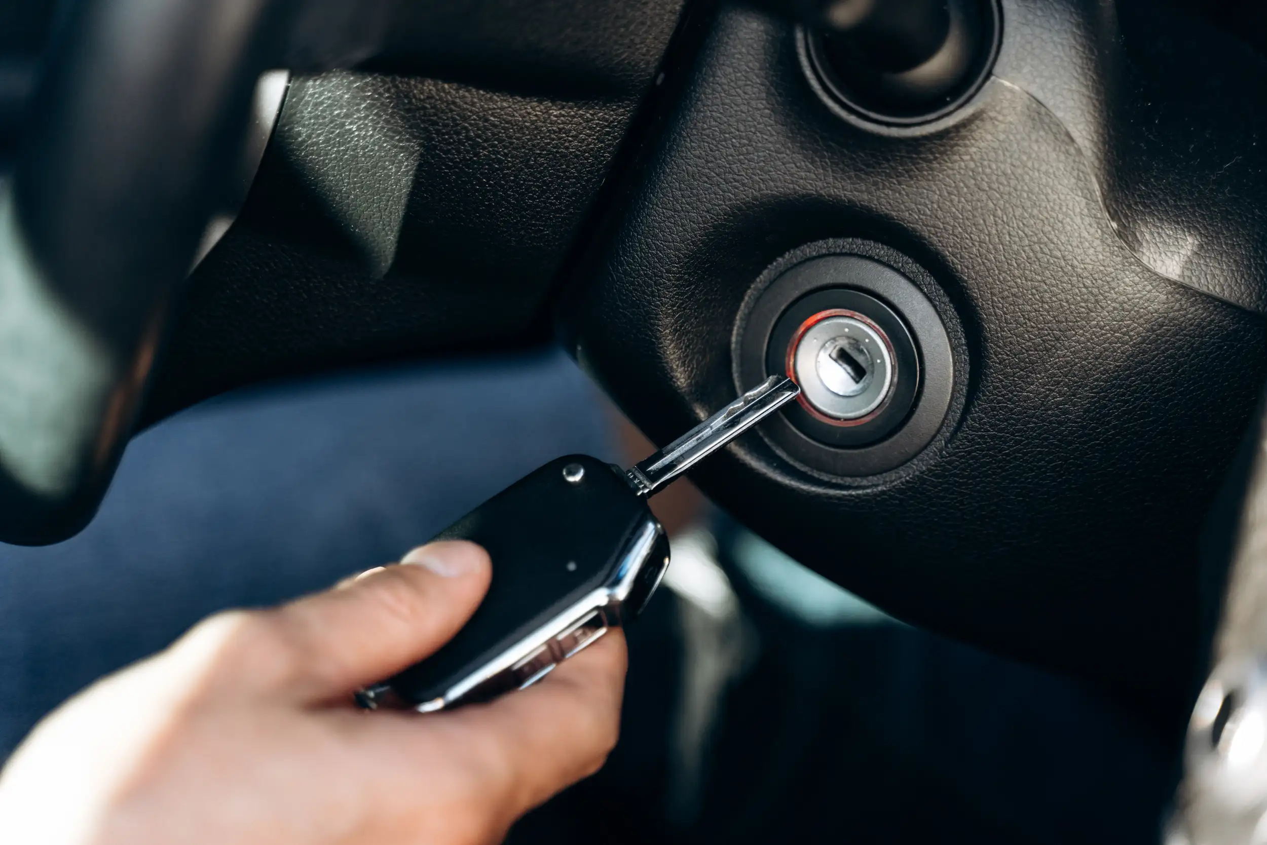Male hand inserting a car key into the ignition, symbolizing auto lockout service and vehicle access assistance.
